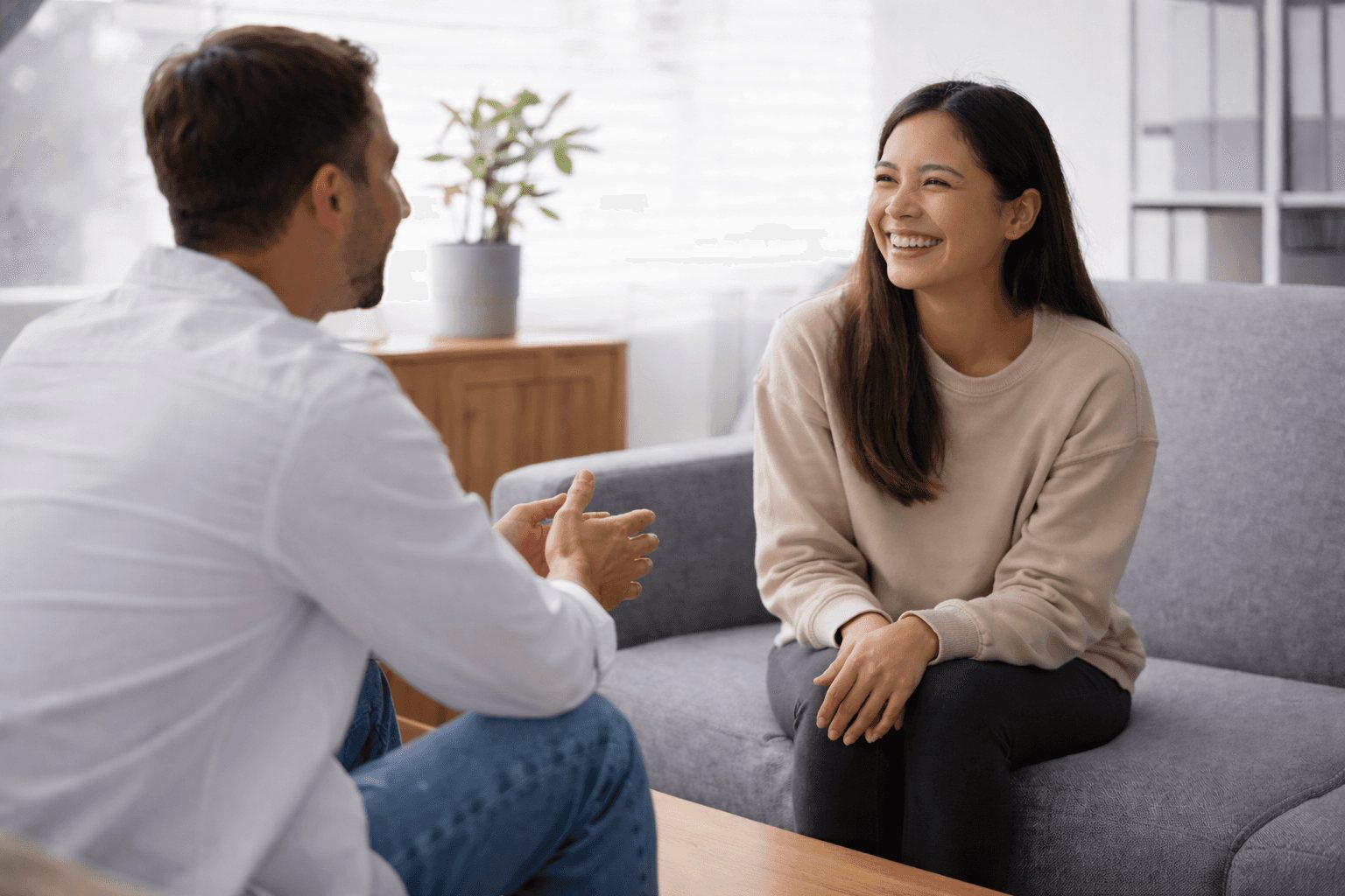 A counsellor and a patient talking together on a sofa in a bright consulting room.