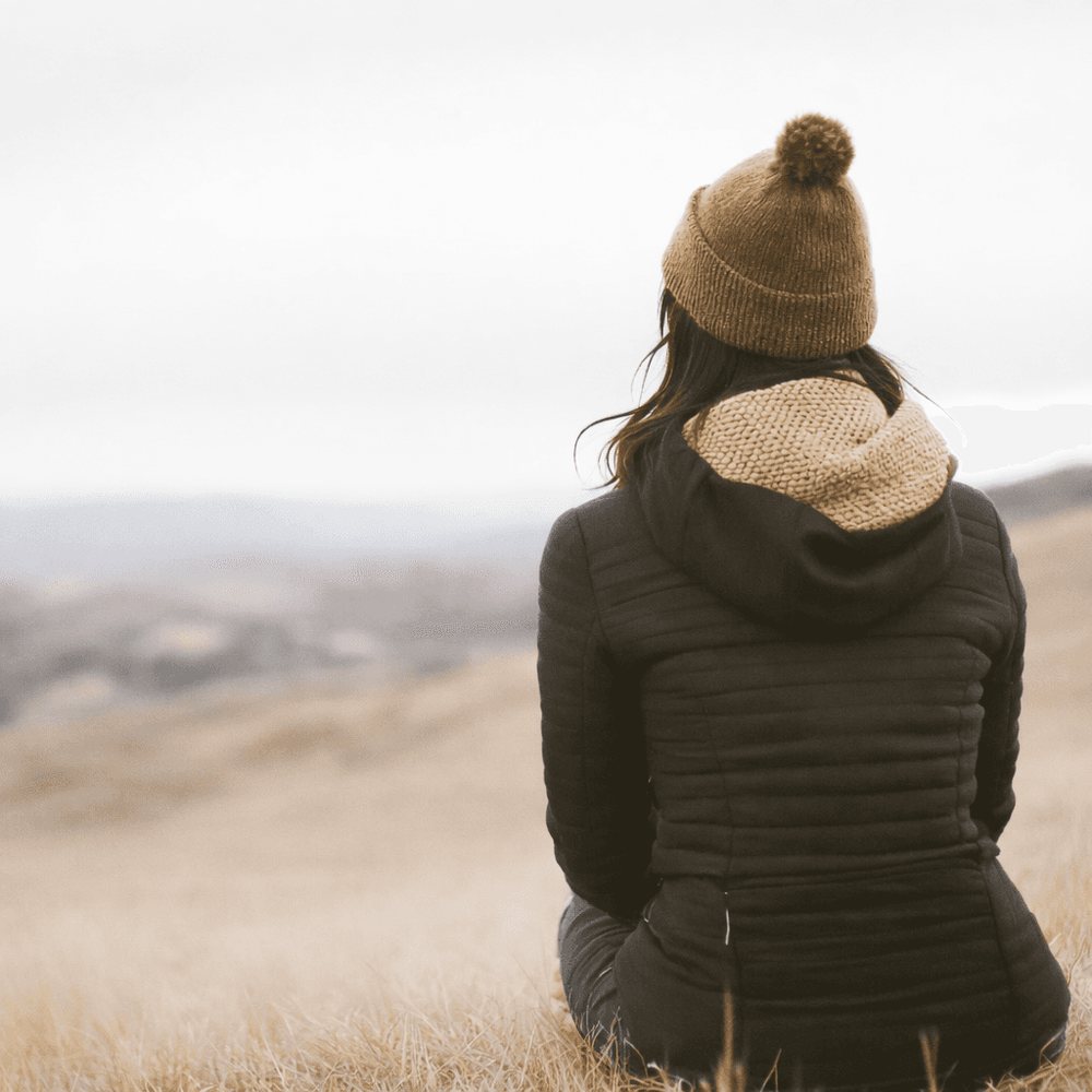 A person sitting outdoors in an open field, looking out toward the hills.